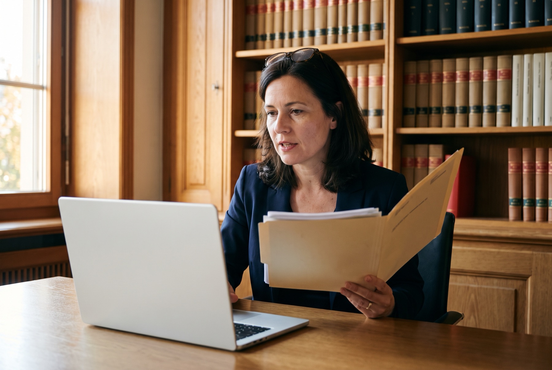 A lawyer dictates at her desk, a case file in her hand.